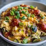 A close-up of a hearty Scrambled Egg and Veggie Bowl, featuring wilted spinach, cherry tomatoes, and gooey melted cheese.