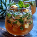 Pineapple Basil Agua Fresca in a clear glass pitcher with ice, garnished with fresh basil and pineapple slices.