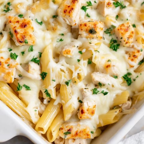 Freshly baked Chicken Alfredo Bake from the oven, steam rising, with golden cheese and fresh parsley garnish.