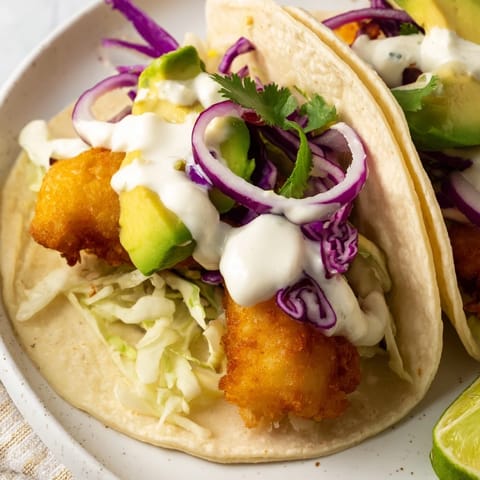 Freshly fried Baja Fish Tacos nestled in warm corn tortillas, topped with creamy lime sauce.