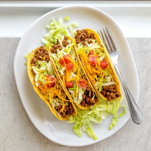 Golden crunchy beef tacos topped with sour cream and fresh cilantro served on a rustic table.