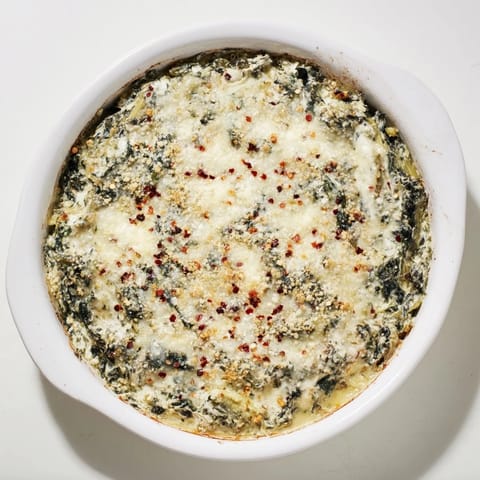 Creamy Spinach Artichoke Dip garnished with fresh spinach leaves, perfect for a game day appetizer spread.