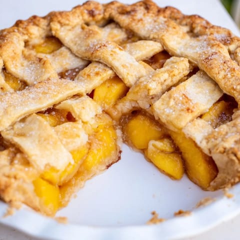 Rustic Peach Pie slice on a white plate with vanilla ice cream melting over the flaky pastry. 