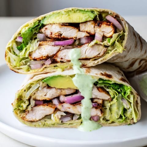 Freshly assembled smoky chipotle chicken wrap with avocado slices, red onion, and drizzled yogurt sauce.  