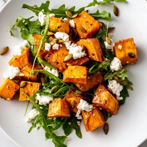 Vibrant roasted sweet potato salad with peppery arugula, red onion, and feta, drizzled with tangy honey-lime dressing.