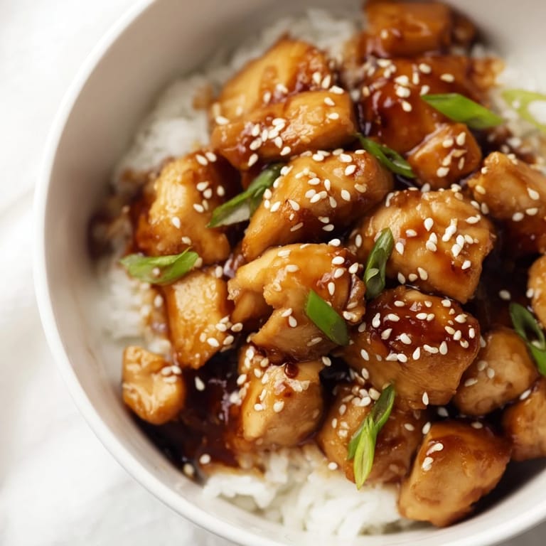 A close-up of tender teriyaki chicken and crisp broccoli in a glossy sauce served over fluffy white rice.