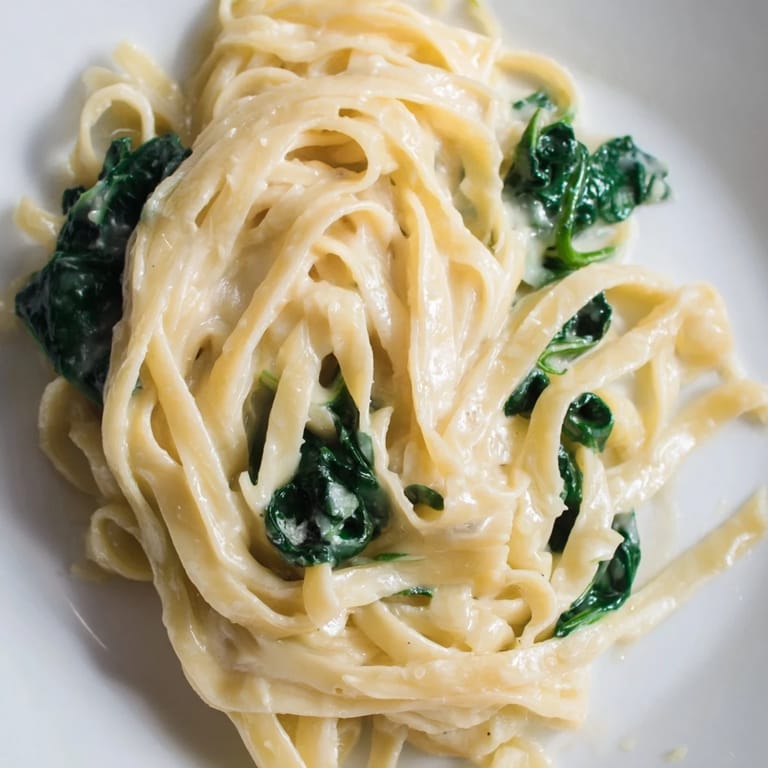 Freshly cooked Creamy Garlic Spinach Pasta garnished with parsley and extra Parmesan, steaming gently on a rustic wooden table for a cozy weeknight dinner.
