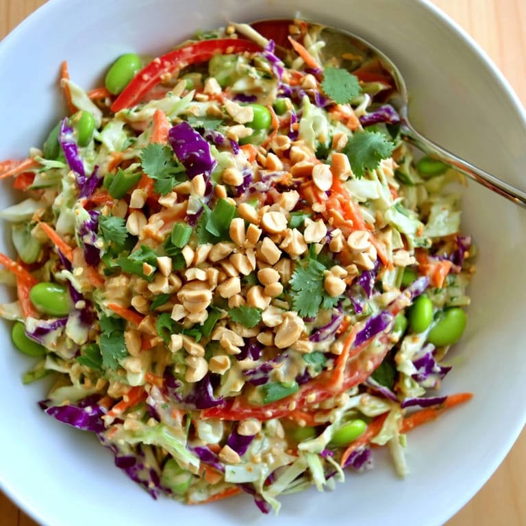 Vibrant Crunchy Thai Peanut Salad in a white bowl, topped with roasted peanuts and sesame seeds, garnished with fresh cilantro and lime wedges.
