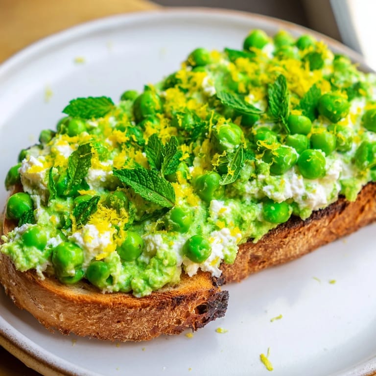 Golden slices of Pea & Mint Ricotta Toast topped with lemon zest and extra peas for brightness.