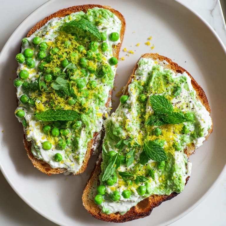 A plated Pea & Mint Ricotta Toast served with lemon wedges and a drizzle of olive oil.