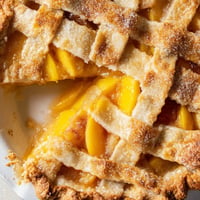 Freshly baked Peach Pie with a golden lattice crust and caramelized peach filling bubbling through the gaps. 